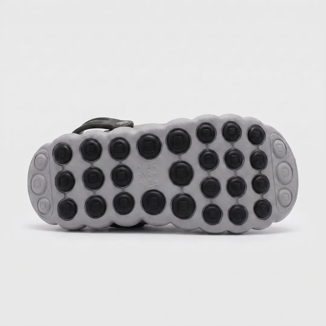 The outsole of a gray and black shoe, showing a pattern of circular black grips on a textured gray base, photographed against a light gray background.